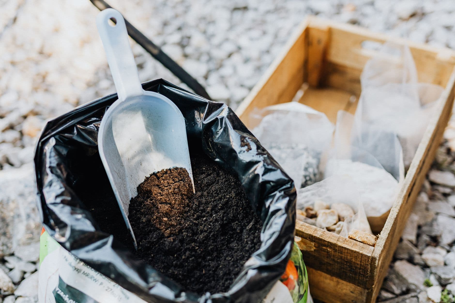 A gardener in gloves spreading black organic substrate while planting a seedling in a garden